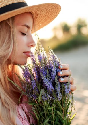 Romantic close up portrait  o charming blonde girl in straw hat  smells    flowers   on   the evening beach,  Warm sunset colors. Bouquet of lavender. Details.