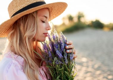 Romantic close up portrait  o charming blonde girl in straw hat  smells    flowers   on   the evening beach,  Warm sunset colors. Bouquet of lavender. Details.