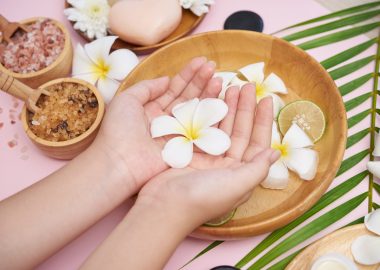 Woman soaking her hands in bowl of water and flowers, Spa treatment and product for female feet and hand spa, massage pebble, perfumed flowers water and candles, Relaxation. Flat lay. top view.